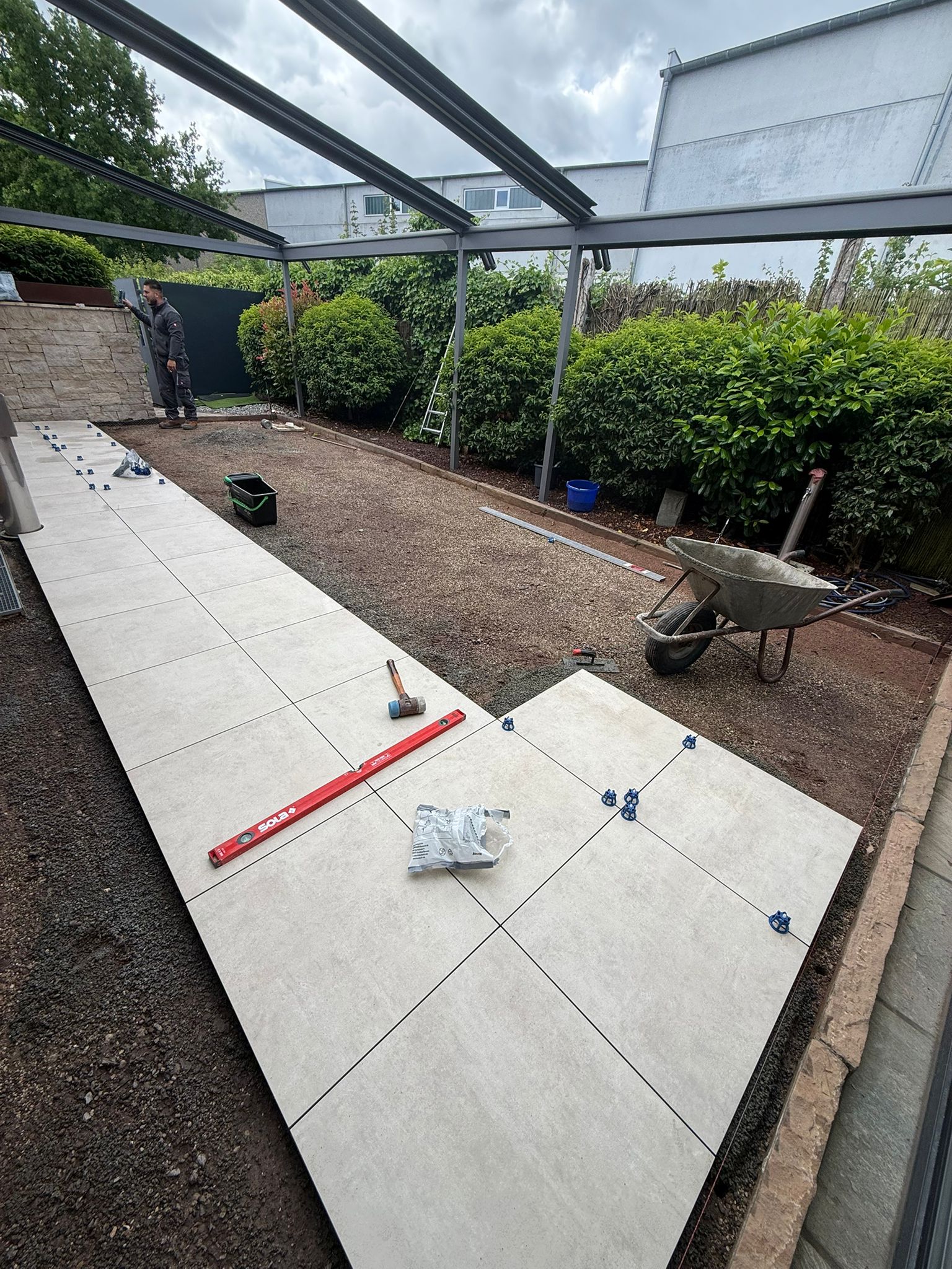 Großformatige Terrassenplatten werden unter einer Pergola verlegt
